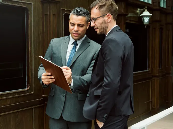 Two businessmen in suits review a clipboard outside an office, discussing services and partnerships via Local Biz Central Now
